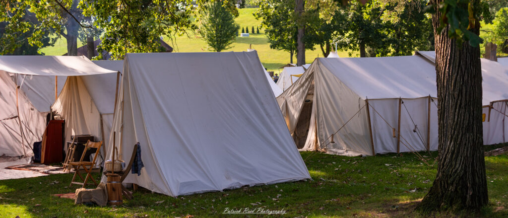 A Union Army encampment in a wooded area, featuring rows of tents set up neatly and campfires smoldering gently. The scene captures the essence of military life during the Civil War, with equipment and personal belongings arranged around the camp, creating a peaceful yet poignant atmosphere of a temporary home in the field.
